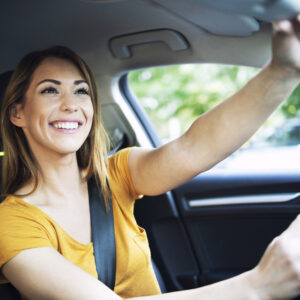 Happy woman adjusting rearview mirror while driving.