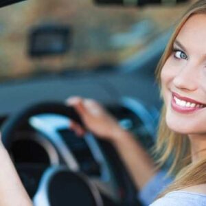 Woman driving car with thumbs-up, smiling confidently.